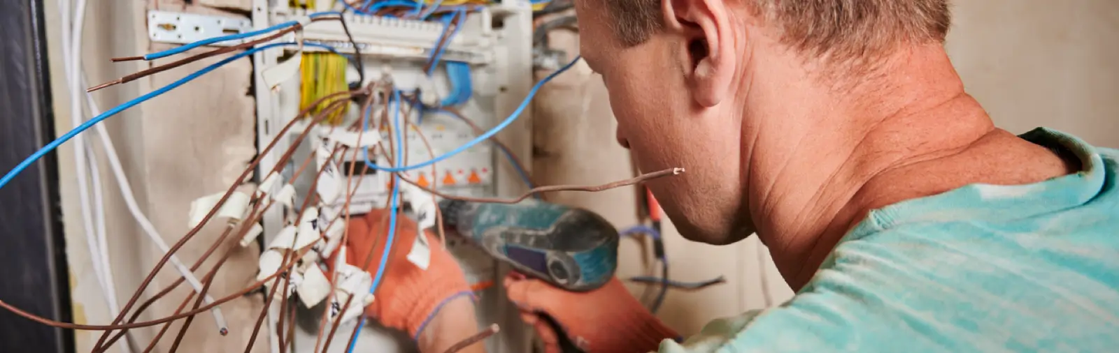An electrician secures a bundle of wires inside an open circuit-breaker panel on an unfinished wall.